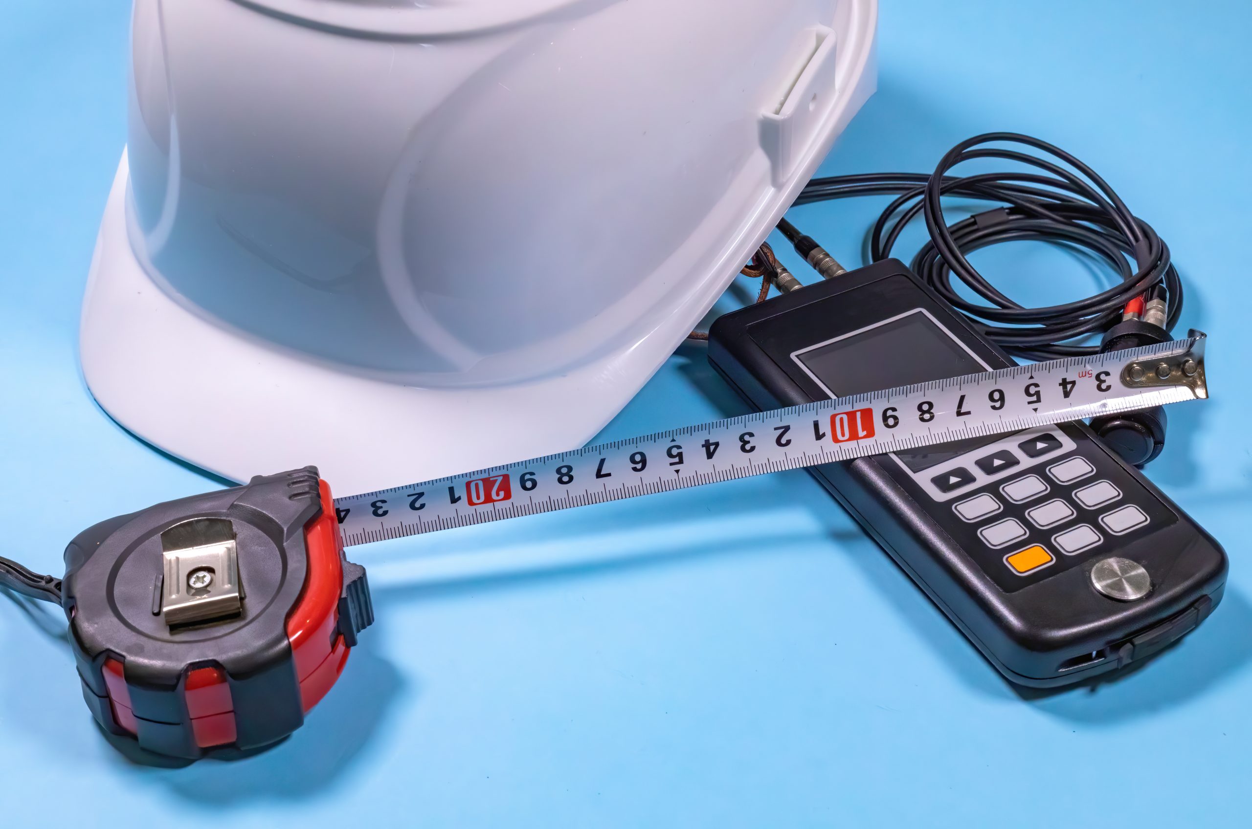 White hardhat, ultrasonic measurement device and a tape-line illustrating non destructive testing procedures (ndt).
